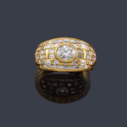 Lote 2143: Anillo con diamante talla oval de aprox. 0,74 ct engastado en bisel con diamantes talla baguette en montura gallonada de oro amarillo de 18K.
