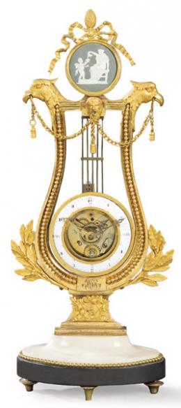 Lote 1244: Reloj esqueleto Luis XVI en forma de lira, en bronce dorado y mármol. Los brazos de la lira sostienen de lo alto dos cabezas de águilas que sostienen en sus picos una cadena.