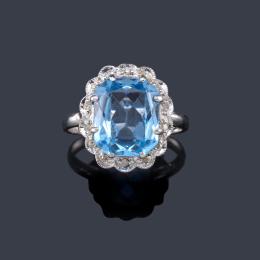 Lote 2182
Anillo con espinela azul sintética con orla de diamantes en montura de oro blanco de 18K.