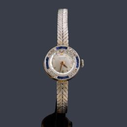Lote 2551: UNIVERSAL de señora con caja y brazalete en oro blanco de 18 K con orla de zafiros y diamantes.