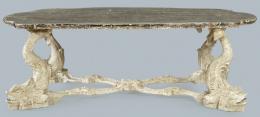 Lote 1106: Mesa de centro con tapa de perfil irregular y lados cónvexos en madera pintada en negro, sobre patas en forma de figuras de peces talladas unidas por chambrana con decoración de roleos tallados en X pintadas de blanco.
Italia, S. XX