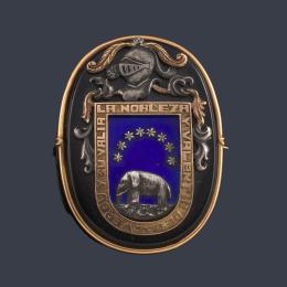 Lote 2011: Broche ovalado con escudo heráldico de la Familia Verdú sobre placa de ónix y esmalte azul en montura de oro amarillo de 18K.