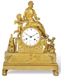 Lote 1022: Reloj de sobremesa Imperio  en bronce dorado, sobre un basamento rectangular se sitúa un plinto cuadrado sobre el que se sienta Psique y a su lado cupido. Junto a el una colmena con abejas. Francia, primer tercio S. XIX