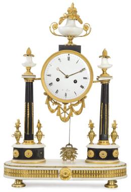 Lote 1484: Reloj de sobremesa de pórtico Luis XVI en mármol blanco, negro y monturas de bronce dorado. En forma de portada sobre zócalo elíptico, dos columnas sobre plintos ovalados y ramatados por copas.