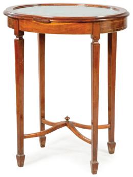 Lote 1043: Mesa expositora eduardina en madera de caoba con embutido de limoncillo, tapa ovalada abatible, sobre patas en estípite unidas por chambranas. Inglaterra, principios S. XX