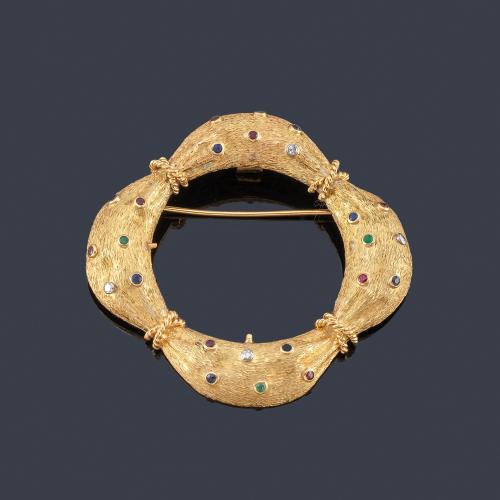  Broche-colgante en forma circular con salpicado de brillantes, zafiros, rubíes y esmeraldas engastados en chatón sobre montura en oro amarillo de 18K con efecto martelé.