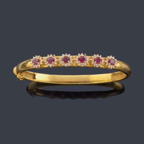  Pulsera rígida con seis rosetones con rubíes talla oval y orla de brillantes, en montura de oro amarillo de 18K.