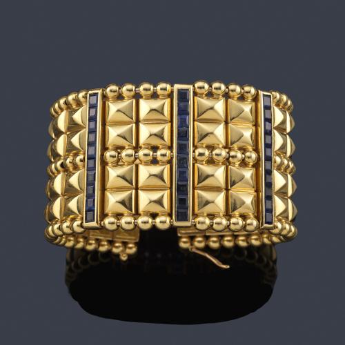  Pulsera ancha y rígida con diseño geométrico y frente con tres bandas de zafiros calibrados en montura de oro amarillo de 18K.