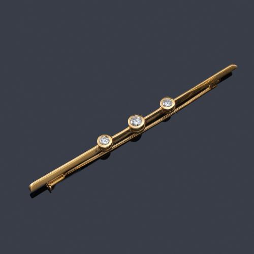  Broche-barrita con tres brillantes engastados en chatón, en montura de oro amarillo de 18K.