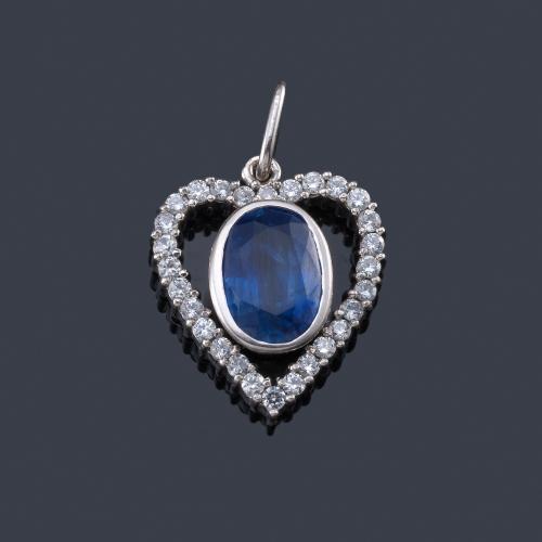  Colgante en forma de corazon con centro de zafiro talla oval y orla de brillantitos en montura de oro blanco de 18K.