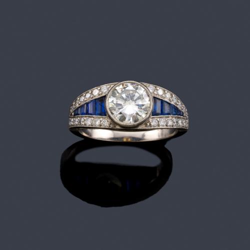  Anillo con brillante central de aprox. 1,35 ct con banda de zafiros de aprox. 0,81 ct en disminución y brillantes de aprox. 0,40 ct en total. 