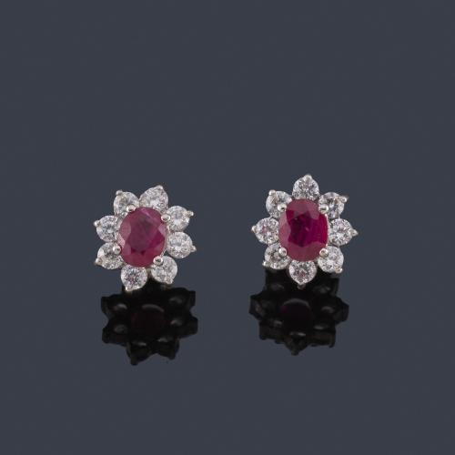  Pendientes cortos con pareja de rubíes talla oval y orla de piedras incoloras, en montura de oro blanco de 18K.