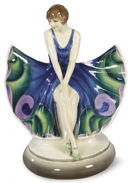  Figura en porcelana de Goldscheider representando una joven sentada con vestido azul, verde y morado. Con sello en la base
Austria, hacia 1930.