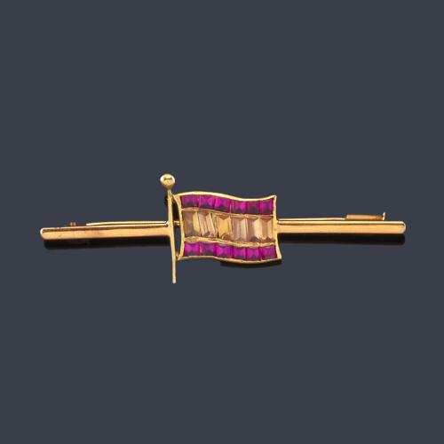 Lote 2515
Alfiler con motivo central de la bandera de España con cuarzo citrinos y rubíes sintéticos.