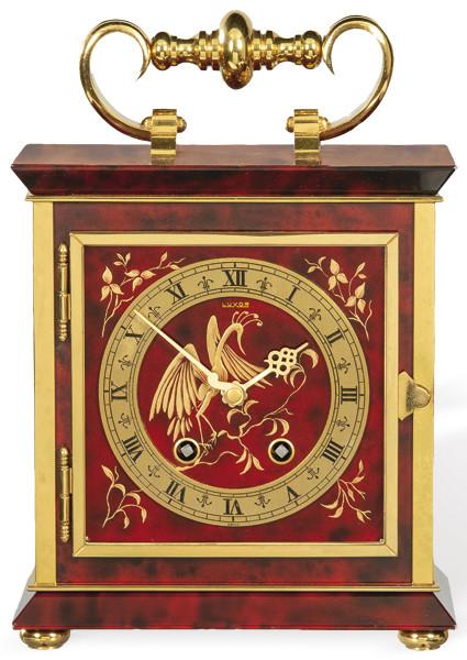 Reloj de sobremesa Luxor con caja de madera y bronce. Esfera redonda con números romanos decorada con un ave y motivos florales. Asa superior en bronce.S. XX