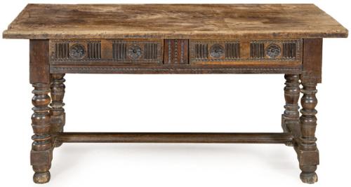 Mesa de tapa rectangular en madera de nogal, con dos cajones en el frente, con decoración tallada, sobre montantes abalaustrados torneados unidos por chambranas rectas.España, S. XVII
