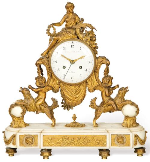  Reloj de sobremesa Luis XVI, sobre basamento elíptico de mármol blanco con bajorrelieves y cortinajes en bronce dorado.