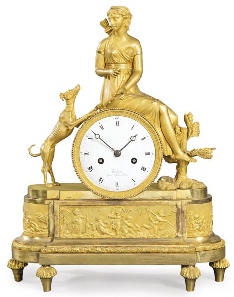  Reloj de sobremesa imperio en bronce dorado. Sobre basamento elíptico se sitúa la esfera del reloj, firmada Brisbart con númeración romana. Encima de ella, Diana cazadora.