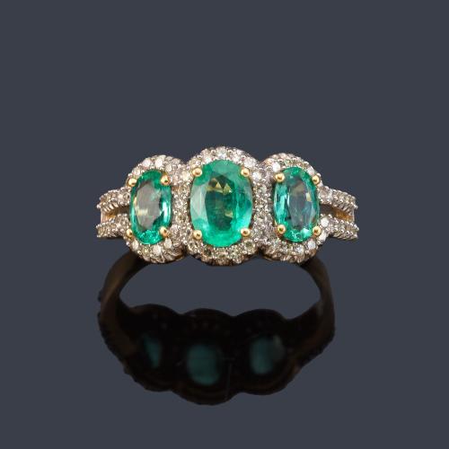 Anillo con tres esmeraldas talla oval y orla de brillantes en montura de oro amarillo de 18K.