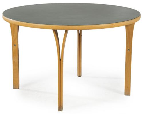  Mesa siguiendo modelos de Rud Thygesen y Johnny Sørensen para Magnus Olesen, con tapa circular en linoleo gris, y estructura en madera de abeto, con patas formadas por dos listones de madera separados en la parte superior.