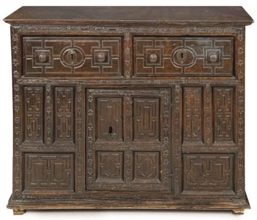 Taquillón en madera nogal, con tapa rectangular moldurada, con dos cajones cortos y profundos en la cintura y en la parte inferior una puerta abatible, con decoración tallada de tipo arquitectónico.