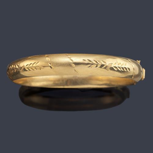 Brazalete rígido de media caña con motivos vegetales cincelados en montura de oro amarillo de 18K.