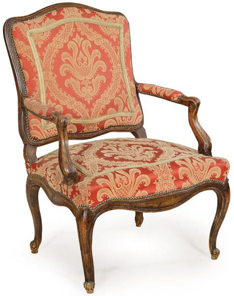 Butaca Luis XV en madera de nogal tallada, con tapicería de tela roja y dorada.
