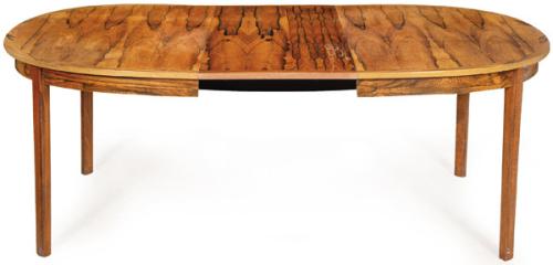 Mesa de comedor extensible, con tapa ovalada en madera de palisandro, sobre patas rectas.