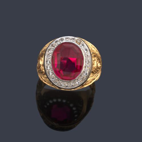 Anillo tipo sello con rubí sintético talla oval facetado con orla de brillantes en montura de oro amarillo de 18K cincelado y vista en oro blanco.