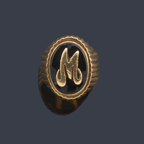 Anillo con letra 'M' sobre placa de ónix en montura de oro amarillo de 18K.