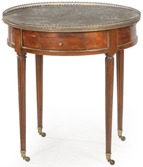 Gueridon Luis XVI en madera de caoba, con tapa de mármol, sobre patas acanaladas terminadas en ruedas y aplicaciones de bronce. Francia, finales S. XVIII