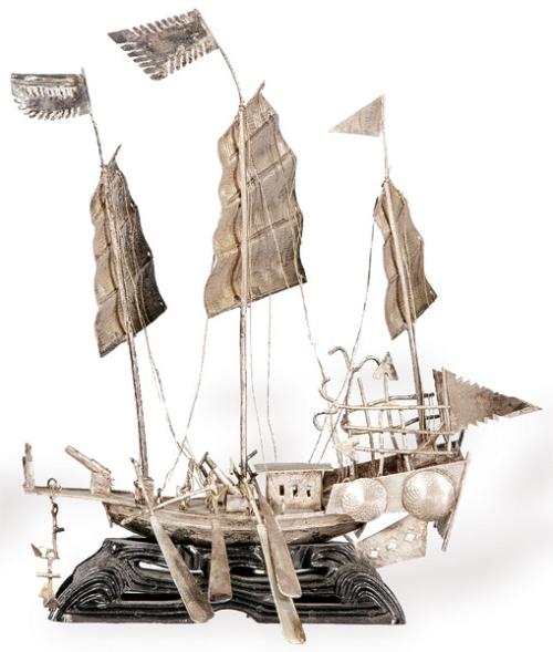 Barco chino de plata sobre peana de madera.