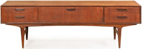 Aparador bajo en madera de teca, con cuatro cajones cortos y uno ancho central con tiradores tallados, sobre patas tronco piramidales. 
