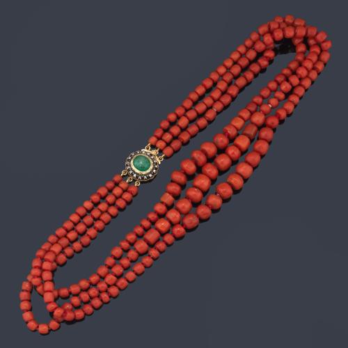 Collar con tres hilos de cuentas de coral rojo facetadas con broche en oro amarillo de 18K, esmeralda talla cabujón y orla de diamantes talla rosa. Ppios S. XX.