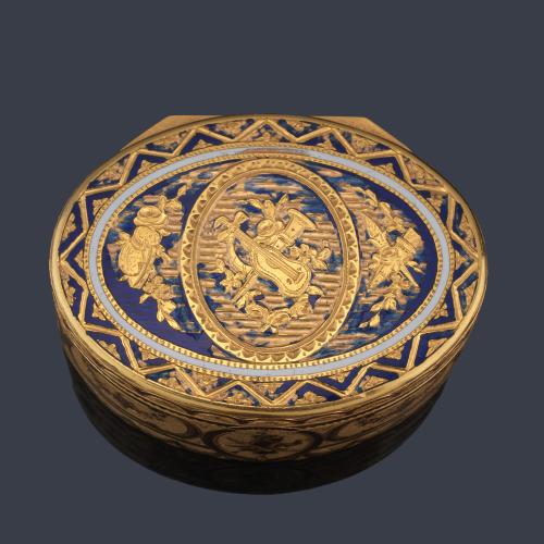 Caja de rapé ovalada realizada en oro amarillo de 20K con motivos de instrumentos musicales en la parte superior cincelado en el oro, enriquecido con esmalte azul y marfil. S. XIX.