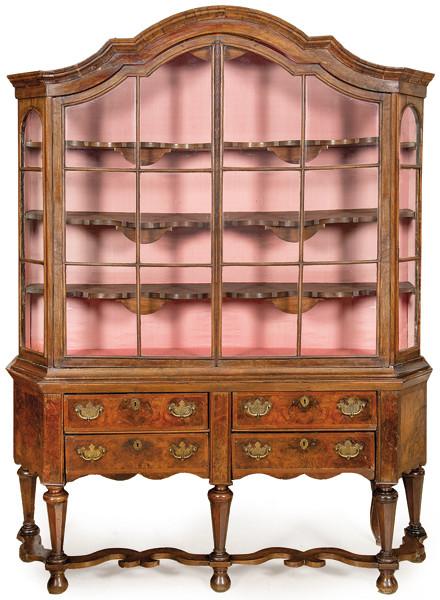 Cabinet on stand barroco en madera de nogal con cornisa moldeada en forma de serpentina sobre puertas acristaladas y cuatro cajones cortos con tiradores en bronce, en patas facetadas unidas por chambrana recortada, y pies de moño.