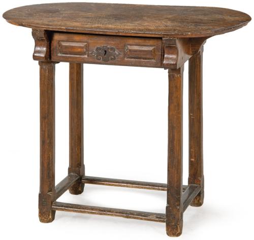 Mesa con tapa elíptica, sobre peinazos recortados en forma de voluta y patas rectas facetadas en madera de nogal, unidas por chambranas.