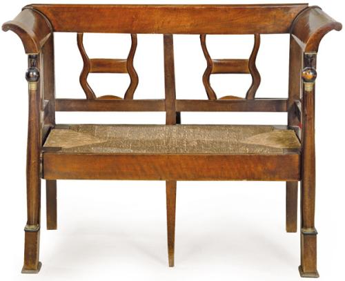 Pequeño canapé fernandino en madera de caoba, con respaldo calado y recortado, el frente de las patas delanteras en forma de columnas toscanas torneadas con basas y capiteles en latón. Asiento de enea. España, primer tercio S. XIX