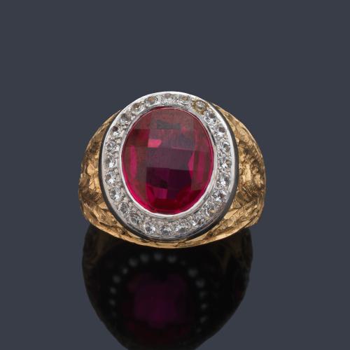  Anillo tipo sello con rubí sintético talla oval facetado con orla de brillantes en montura de oro amarillo de 18K cincelado y vista en oro blanco.