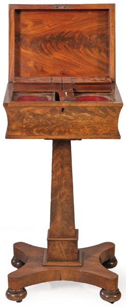 Teapoy William IV en madera de caoba y palma de caoba, con tapa abatible que rebela un interior con huecos para colocar las cajas de té, sobre pedestal de sección cuadrada, sobre plataforma de cuatro lados cóncavos apoyada en ruedas. Inglaterra, h. 1830