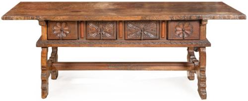 Mesa con tapa enteriza rectangular en madera de nogal, sobre montantes rectos, en la que se ensamblan dos grandes peinazos en forma de ménsulas; entre los que se alojan los cajones con talla de tipo vegetal.