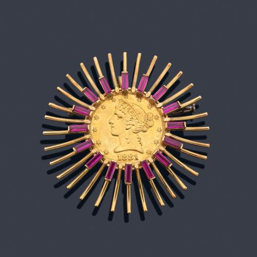 Broche con moneda central de cinco dólares de 22K con diseño en forma de sol enriquecido con rubíes sintéticos talla rectangular, sobre montura de oro amarillo de 18K.