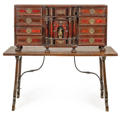  Bargueño Carlos II en madera de nogal, madera ebonizada y carey, con monturas de bronce. Con una portada central de puerta abatible flanquea 4 cajones a cada lado. Sobre mesa con patas recortadas y fiadores de hierro.