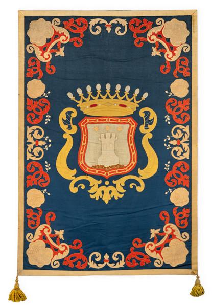 Repostero con escudo rematado por corona condal sobre campo azul en lana, enmarcado por motivos vegetales en rojo y dorado.