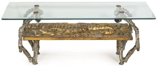  Mesa de centro, con tablero rectangular de vidrio templado, apoyado sobre estructura escultórica en metal fundido con acabado dorado y patas en metal plateado de sección irregular. Base decorada en relieve con composición figurativa.