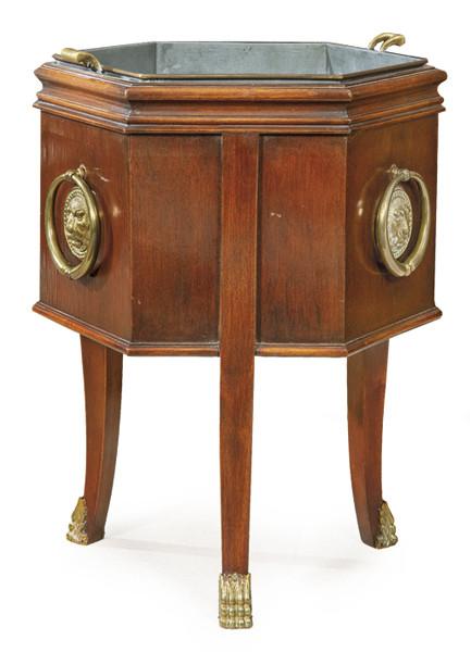  Jardinera Regencia con estructura hexagonal en madera de caoba con decoración moldurada, sobre patas en estípite acabadas en garras de animal en bronce al igual que las asas laterales. Protector interior de estaño. Inglaterra, finales S. XVIII