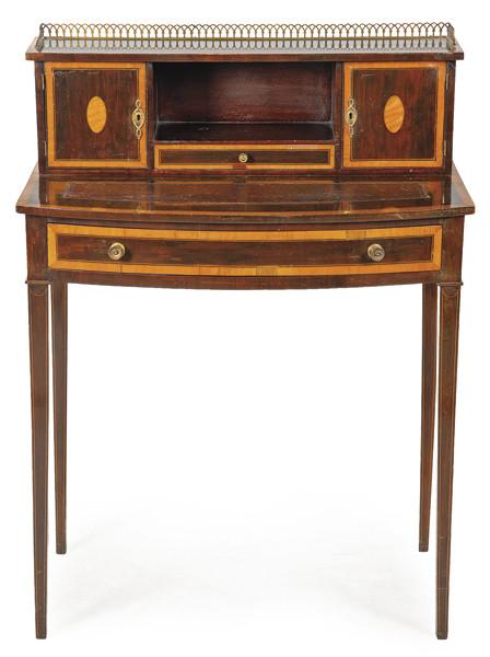 Pequeño escritorio eduardino siguiendo modelos regencia en madera de caoba y satin wood, con el frente ligeramente curvo. Tiradores y barandilla de latón. 