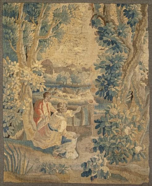  Tapiz verdure tejido en lana y seda, de composición vertical con paisaje frondoso organizado mediante un gran arbolado que enmarca la escena del primer término en la que se representa una pareja conversando. 