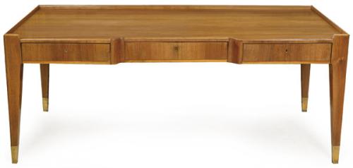  Mesa de escritorio en madera de nogal, con el sobre, de canto recto y sin vuelo, descansa sobre un bastidor frontal integrado por tres cajones enrasados sin tiradores. Las patas piramidales se prolongan hasta el suelo rematadas en conteras troncocónicas d