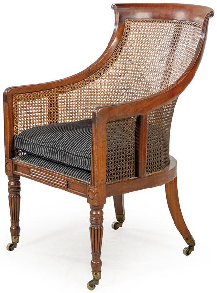 Butaca Jorge III en madera de caoba, con respaldo alto curvo y reposabrazos envolventes, con canto acanalado y rejilla.